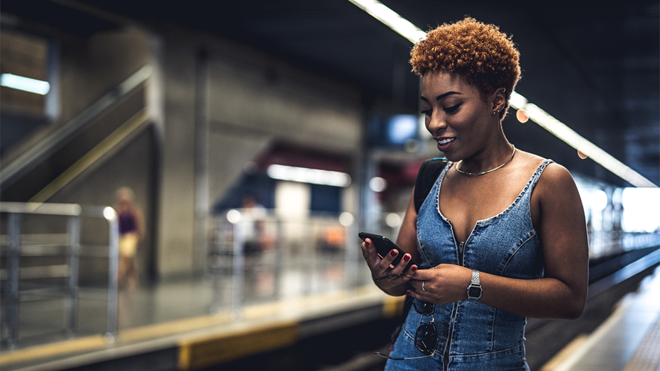 Jovem em plataforma da CPTM aguardando o trem enquanto visualiza o celular