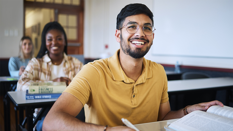 Foto de uma sala de aula como fundo e em destaque um jovem sorrindo enquanto estuda.