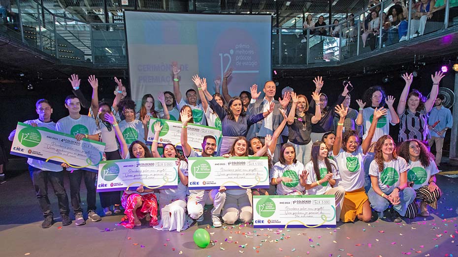 Foto de um palco com um grupo de pessoas comemorando. Alguns estão segurando um cheque simbólico.
