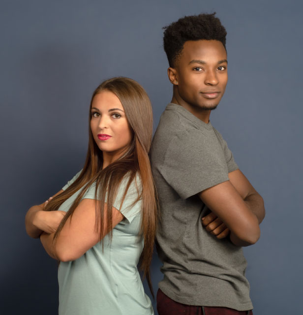 Foto de dois jovens, uma moça branca e um rapaz negro de braços cruzados